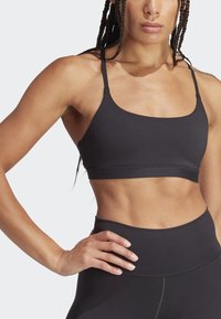 Crni sportski crop top s tankim trakicama, izrađen od glatkog, mekanog materijala. Ima široki pojas ispod grudi i kvadratni izrez.