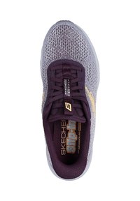 Zapatilla deportiva con parte superior de malla en gris, acentuada por un sistema de cordones y un logo en púrpura intenso. Cuenta con una plantilla acolchada y diseño sin cordones para calzar fácilmente.