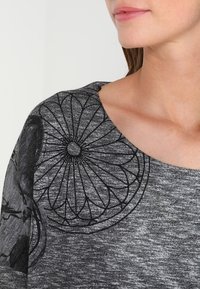 Grauer, texturierter Pullover mit schwarzer Blumenstickerei auf der Schulter. Verfügt über einen weiten Ausschnitt und einen weichen Stoff, der für Komfort sorgt.
