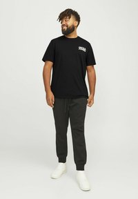Schwarzes Baumwoll-T-Shirt mit weißem Logo auf der Brust, kombiniert mit schwarzen Jogginghosen und weißen Sneakers, ausgestattet mit einem elastischen Bund.