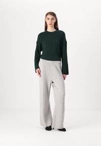 Maglione verde a maglia con texture a coste abbinato a pantaloni a gamba larga grigio chiaro con motivi a coste verticali e vestibilità rilassata.