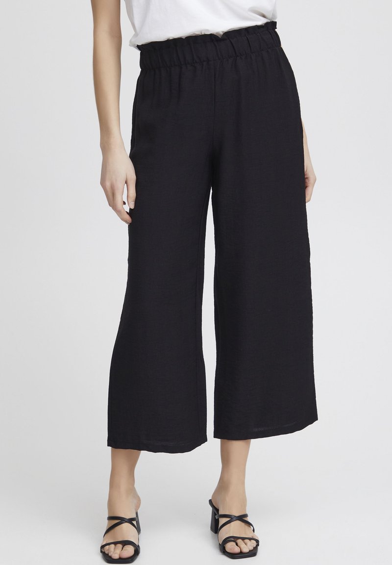 Zwarte wijde broek met een textuurstof, voorzien van een elastische tailleband en een comfortabele pasvorm. Gepaard met zwarte sandaal met bandjes.