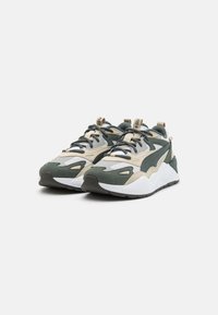 Baskets vertes et beiges avec un mélange de matériaux en maille et en daim. Elles présentent une épaisse semelle blanche, une forme arrondie et des détails de couture contrastés.