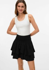 Svart lagdelt skjørt med smocket liv, laget av lett stoff. Har en avslappet, utsvungen design som gir volum og bevegelse.