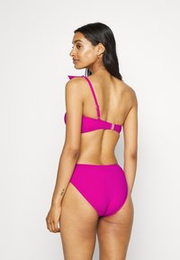 Completo bikini rosa con top strutturato e spalline regolabili e pantaloni a vita alta. Texture liscia con dettagli hardware minimi.
