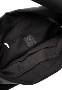 Intérieur d'un sac en tissu noir avec une poche zippée. Dispose d'une étiquette en cuir noir texturé avec un design en relief. Texture lisse et design sans couture.