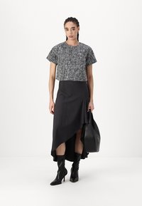 Top nero e bianco con texture, corto e a maniche corte, abbinato a una lunga gonna scura asimmetrica e stivali neri fino al ginocchio. Porta una borsa nera.