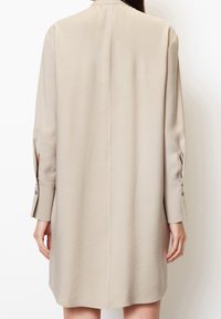 Beige Langarmkleid mit geradem Schnitt, geknöpften Manschetten und glatter Textur. Es verfügt über eine zentrale Naht entlang des Rückens.