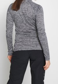 Langärmliges Sportoberteil aus meliertem grauem Stoff mit hohem Kragen und figurbetontem Design, von hinten gezeigt. Kombiniert mit schwarzen Unterteilen.