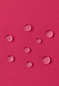 Un tessuto fucsia con una trama a texture presenta diverse gocce d'acqua chiare che riposano sulla sua superficie, evidenziando le sue proprietà impermeabili.