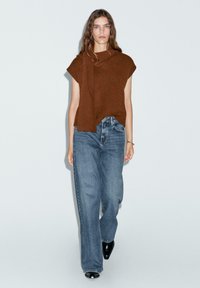 Top in maglia marrone con scollo drappeggiato, abbinato a jeans a gamba larga blu chiaro e stivali con tacco neri. Tessuto semplice e strutturato in una vestibilità comoda.