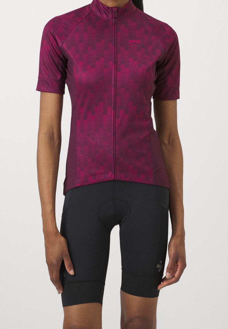 Krátký cyklistický dres s rukávy v tmavě magentové barvě s geometrickým vzorem, s předním zipem a slim fit střihem, doplněný černými cyklistickými šortkami.