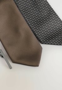 Trois cravates : une cravate marron texturée, une cravate noire à motifs avec des accents bleus et un pince-cravate en argent à gauche.