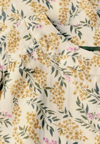 Tissu floral présentant des grappes de fleurs jaune doré et des feuilles vertes sur un fond crème, avec des accents roses subtils et une texture douce.