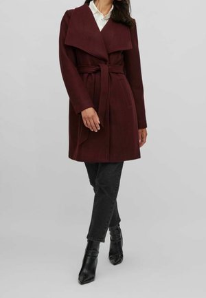 Burgundy wool coat with a wide collar, belted waist, and side pockets, paired with black jeans and pointed ankle boots.