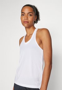 White athletic tank top with a scoop neckline and thin straps. Made from a textured fabric with a small logo at the hem.