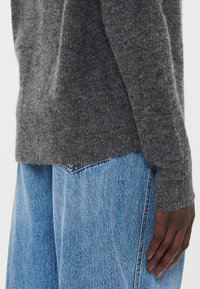 Grå strikkegenser med teksturert finish, med lange ermer og rundet kant, sammen med lyseblå denimjeans.