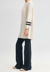 Maglione beige a maglia con motivo geometrico e maniche a tre quarti, caratterizzato da strisce nere sui polsini. Abbinato a pantaloni neri a campana.