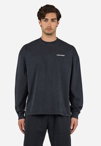 Dark gray long-sleeve sweatshirt made of cotton with a crew neck, featuring a small white "PEGADOR" logo on the chest. Simple design.