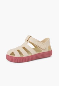 Beige rubber sandal with a pink sole, featuring open cutouts, an adjustable strap, and "Igor" branding on the side. Textured sole.