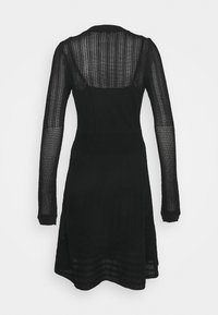 Robe noire en maille avec des manches longues, présentant un design texturé, un buste ajusté et une jupe évasée avec des motifs rayés à l'ourlet.