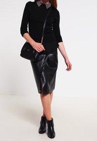 Pullover nero con colletto di perle, abbinato a una gonna a tubino in pelle nera con spacco laterale. Gli accessori includono una piccola borsa nera e stivaletti.