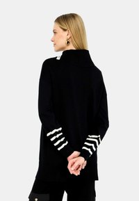 Maglione nero a maglia con colletto alto, caratterizzato da accenti a strisce bianche e crema sui polsini. Vestibilità rilassata e texture morbida.