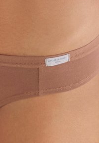 Bruine katoenen ondergoed met een zachte, gladde textuur. Heeft een tailleband met de tekst "intimissimi Natural." Close-up van de stof.