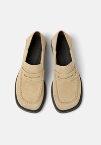 Beige suede loafers with a rounded toe, leather detailing on the vamp, and a black rubber outsole. Subtle stitching accentuates the design.