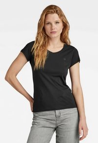 T-shirt preto de manga curta com decote em V, feito de tecido macio, com um design justo e detalhe discreto do logo no peito. Jeans cinzentos Eduard.