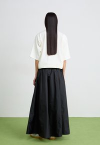 Fehér, oversized, rövid ujjú felső, amelyet egy hosszú fekete szoknyával párosítottak. Simább anyag, laza fazon és széles derékpánt. Hosszú, egyenes haj látható.