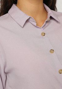 Camisa de botones de lavanda clara con una textura suave, que presenta un cuello clásico y tres botones redondos en color Beig.