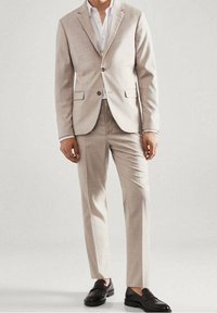 Lichtbeige pak met een geruit patroon, getailleerde pasvorm, enkelvoudig knoopsgat colbert met ingesneden revers en bijpassende broek. Zwarte loafers maken de look compleet.