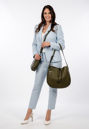 Olive green leather handbag with a rounded shape, drawstring closure, and a detachable strap. Model wears a light blue suit and white heels.