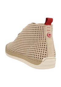 Stivaletti beige alla caviglia in suede perforato, con suola in gomma bianca e un accento rosso sul tallone che presenta un logo. Forma arrotondata con collo basso.