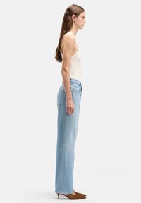 Jeans azzurri chiaro a vita alta con taglio a gamba dritta, realizzati in tessuto denim, abbinati a un top beige aderente e scarpe con tacco marroni.