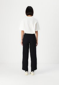 White cotton t-shirt paired with black wide-leg trousers. The outfit is complemented by off-white sneakers with visible branding on the heels.