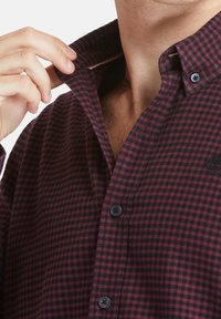 Camicia a quadri button-up in rosso scuro e nero, con colletto, bottoni neri e tessuto testurizzato con una leggera lucentezza.