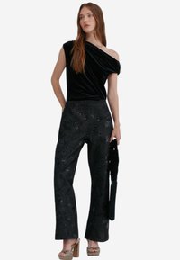 Černý sametový top na jedno rameno spojený s černými širokými kalhotami zdobenými složitými vzory a texturovaným povrchem.