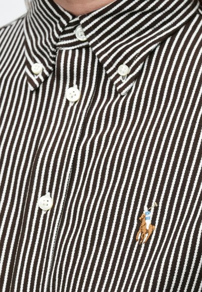 Barna-fehér csíkos gombos ing galléros nyakkal; fehér gombokkal és bal oldali mellrészen hímzett lovas logóval.