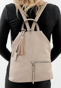 Zaino in pelle beige con frange e cerniera anteriore, indossato da una persona in maglione nero a maniche lunghe visto da dietro.