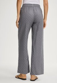 Šedé široké kalhoty s elastickým pasem, s geometrickým vzorem. V kombinaci s minimalistickými černými sandály.