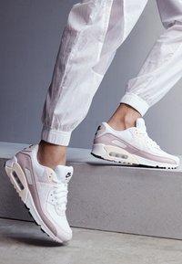 Buty sportowe Nike Air Max 90 w białym i jasnoróżowym kolorze, z cholewką ze skóry, widoczną amortyzacją powietrzną, sznurowanym designem oraz czarną podeszwą.