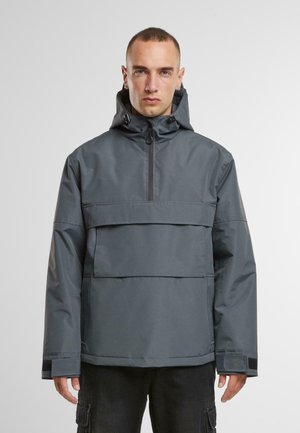 Grå vandtæt jakke med høj krave, halv lynlås, stor frontlomme og elastiske manchetter. Glat tekstur med et holdbart design.
