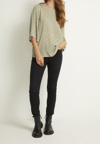 Hellgrüne Bluse mit kleinem weißen Blumenmuster, lockere Passform, aufrollbare Ärmel. Kombiniert mit schwarzen Skinny Jeans und schwarzen Stiefeletten.