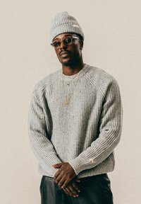 Šedý pletený svetr s ribbovým vzorem a raglánovými rukávy, doplněný odpovídající čepicí. Zlatý náhrdelník s přívěskem, vrstvený s dalším náhrdelníkem.