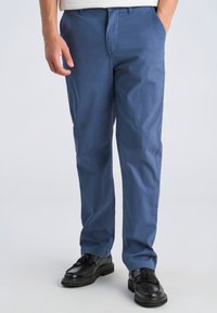 Pantaloni di cotone blu con vestibilità dritta, dotati di tasche laterali e una texture liscia, abbinati a scarpe nere.
