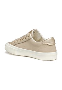 Beige canvas sneakers med en glatt finish, rund tå, gulde øyeeletter, hvit gummisåle og en liten hælforsterkning. Enkelt, minimalistisk design.