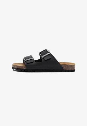 Czarna klapka na płaskiej podeszwie z dwoma regulowanymi srebrnymi klamrami, korkową wkładką i fakturowaną czarną gumową podeszwą, widoczna z boku.