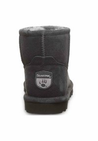 Schwarze Wildleder-Ankle-Boots mit abgerundetem Schaft, weichem Futter und einem kreisförmigen grauen Logo-Patch auf der Rückseite. Flache Gummisohle.